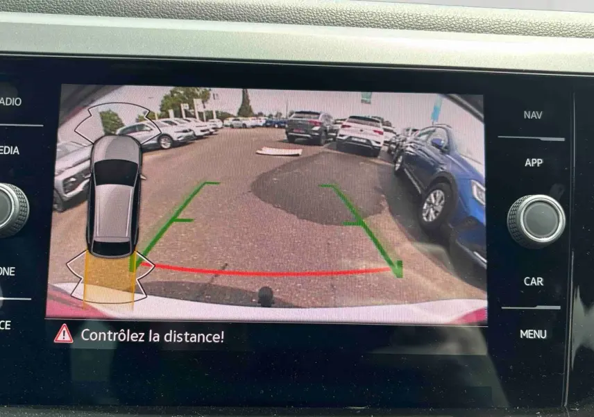 Vue écran caméra de recul du Volkswagen Taigo blanc, avec guidage de trajectoire et alertes de distance visibles.