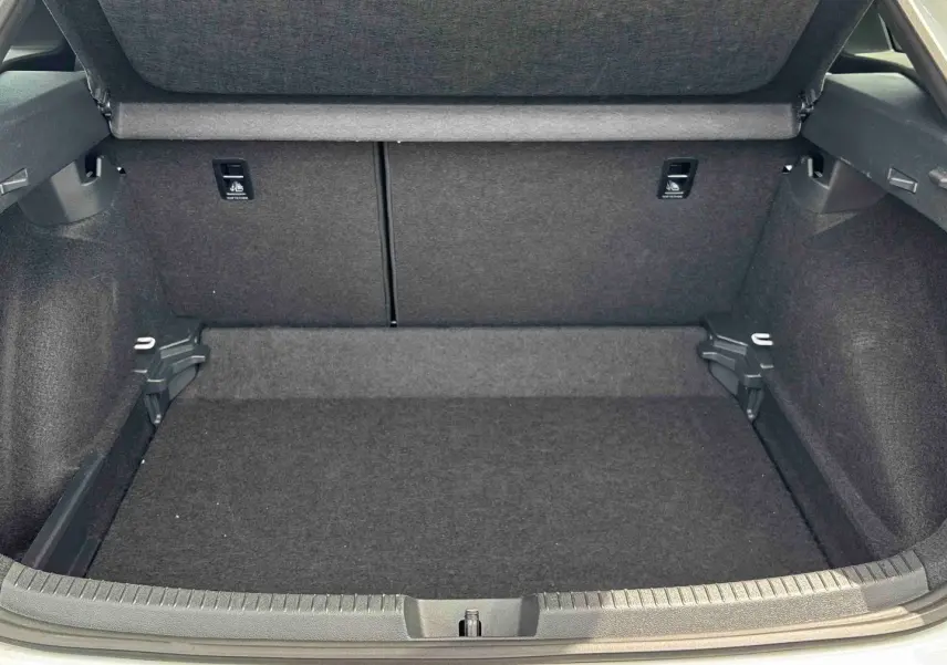 Coffre ouvert vu de l'arrière d'un Volkswagen Taigo blanc, montrant l'espace de chargement vide et la moquette grise.