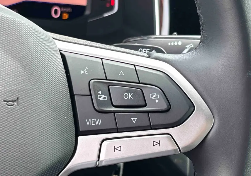 Gros plan sur les commandes multifonctions du volant cuir noir du Volkswagen Taigo 2025, côté gauche.