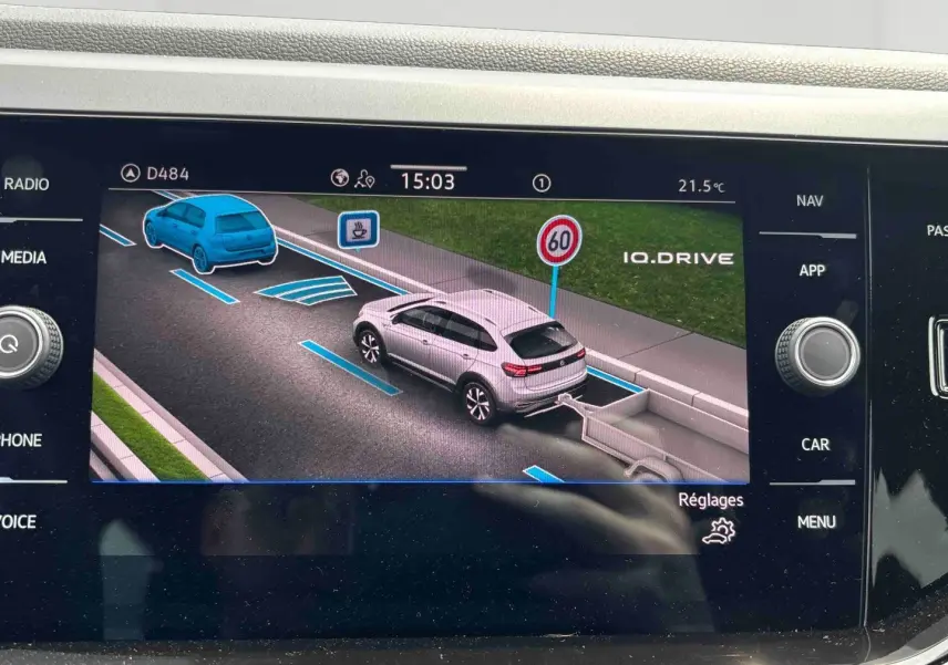 Écran tactile montrant une vue 3/4 arrière d’un Volkswagen Taigo blanc avec attelage sur route et panneau 60 km/h.