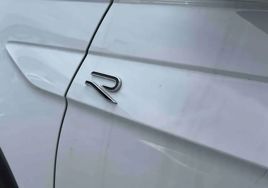 Détail du logo R sur la porte côté gauche d’un Volkswagen Taigo blanc, soulignant la finition R-Line.