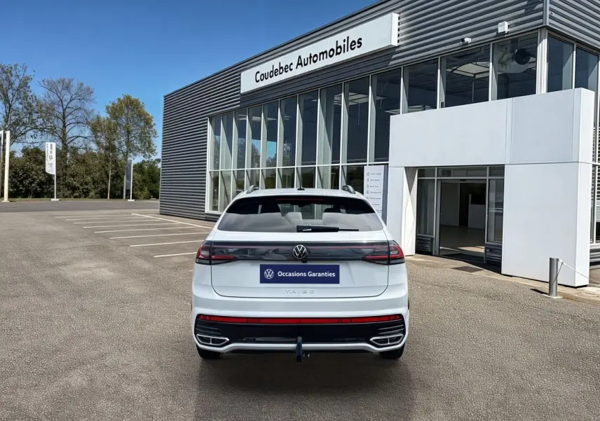 Vue arrière d’un Volkswagen Taigo blanc 2025 avec attelage amovible, garé devant un bâtiment de concession.