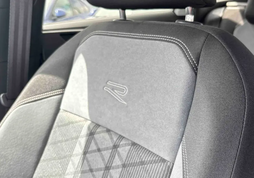 Gros plan sur le siège avant gris foncé avec logo R-Line embossé, coutures blanches et motif géométrique.