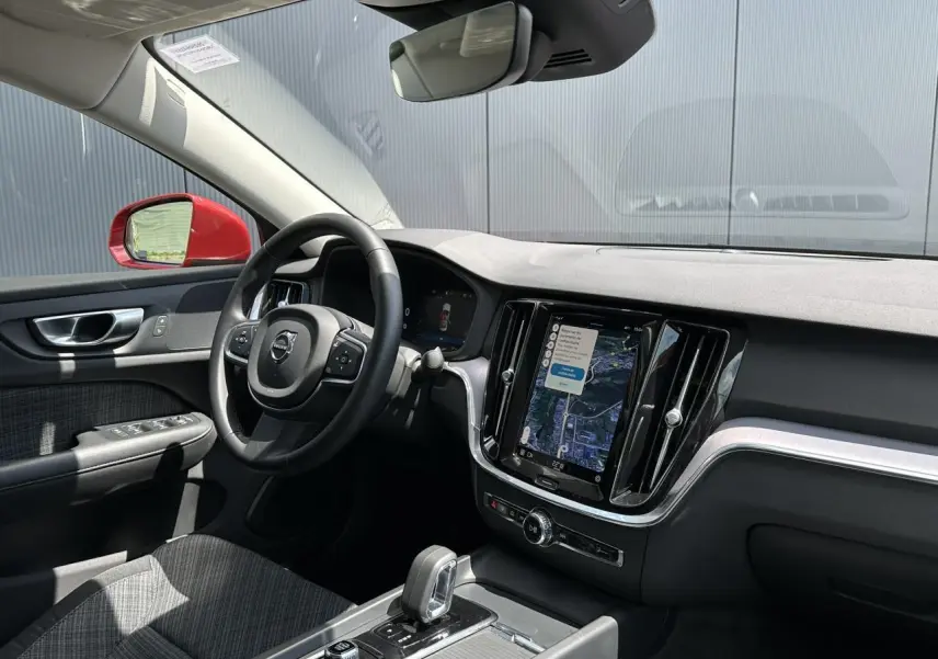 Vue intérieure côté conducteur du tableau de bord et volant noir du Volvo S60 rouge avec écran tactile GPS central.