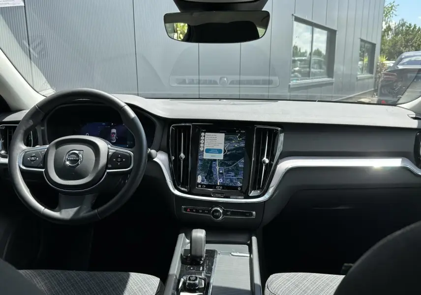 Intérieur avant de la Volvo S60 2024 rouge Fusion, tableau de bord avec écran tactile vertical et volant multifonction.