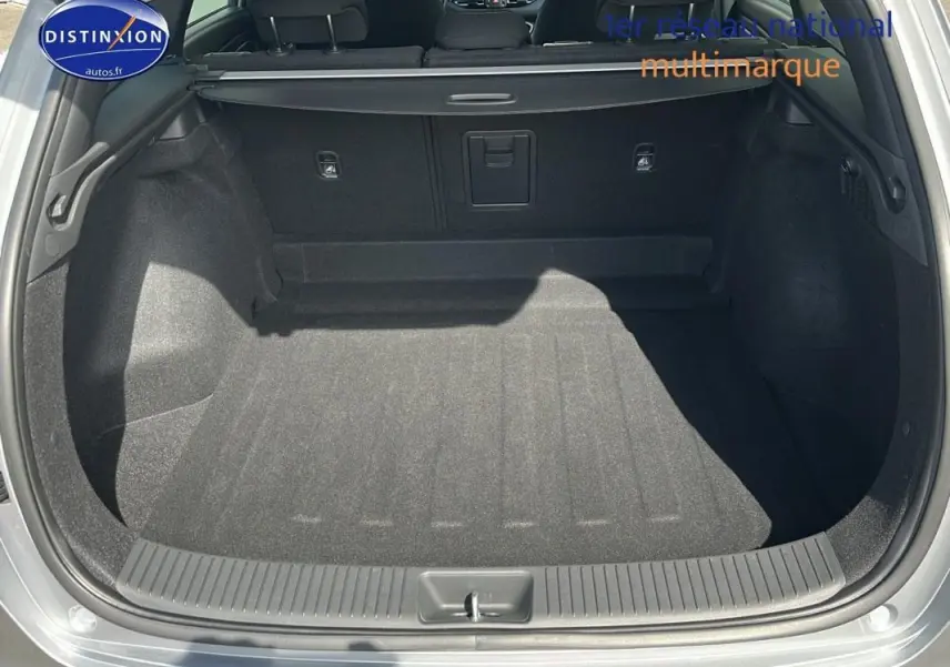 Coffre ouvert d'une Hyundai i30 SW gris clair, vue arrière montrant l'espace de chargement et la plage arrière.