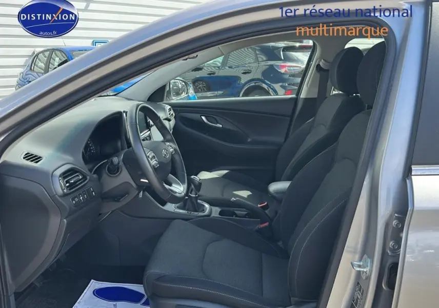 Intérieur de la Hyundai i30 SW gris clair 2022, vue côté conducteur avec sièges noirs et volant multifonction.