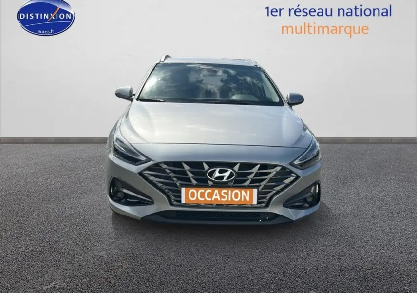 Vue frontale d'une Hyundai i30 SW gris clair avec calandre large et feux LED fins, en extérieur sur sol bitumé.