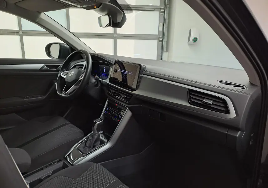 Intérieur du Volkswagen T-Roc 2024 vu côté conducteur, tableau de bord moderne avec écran tactile et volant multifonction noir.
