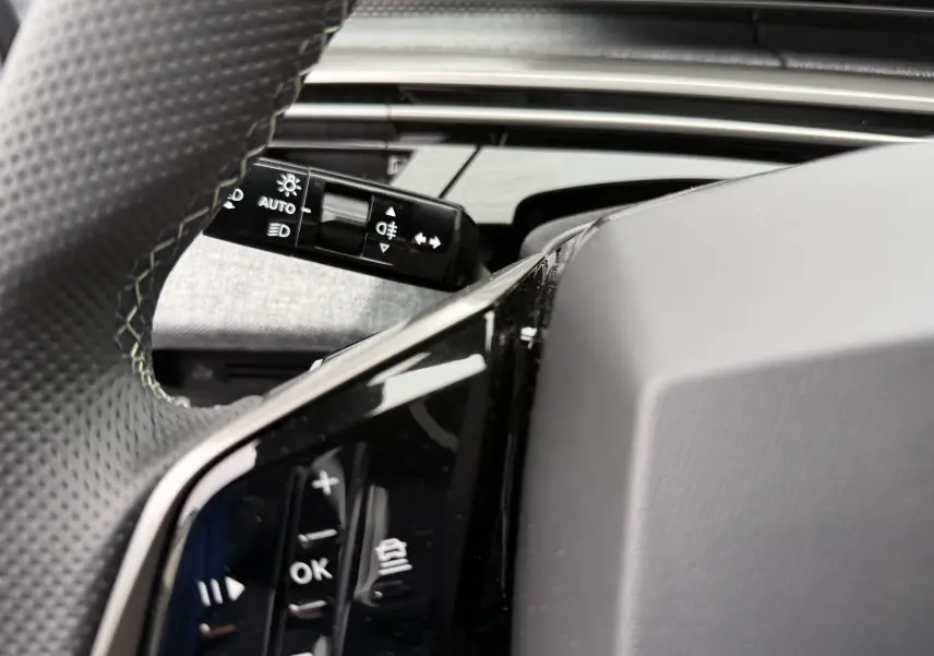 Gros plan sur les commandes au volant du Peugeot 3008 Hybrid blanc, mettant en valeur les boutons de réglage et le commodo d'éclairage.