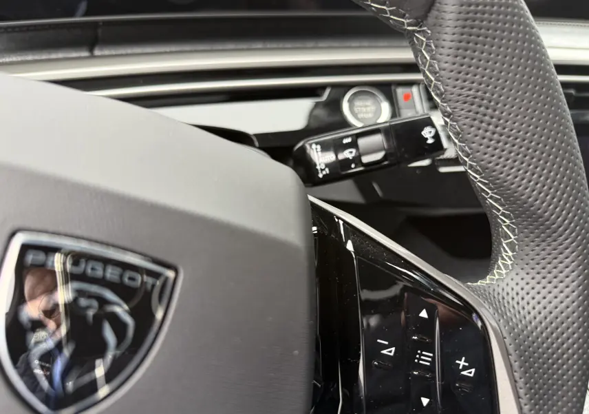 Gros plan sur le volant noir perforé du Peugeot 3008 Hybrid 2025 avec commandes intégrées et logo au centre.