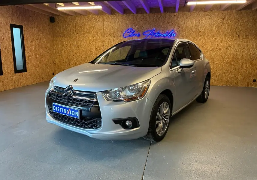 Vue 3/4 avant d'une DS4 gris clair, avec calandre chromée et jantes alliage dans un showroom au mur bois.
