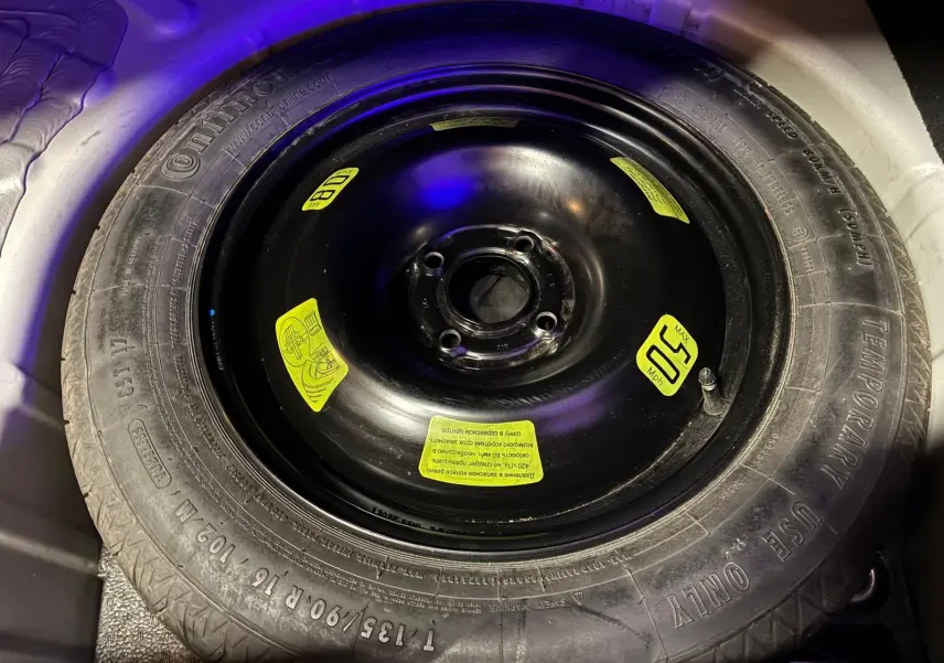 Gros plan sur la roue de secours noire avec étiquettes jaunes dans le coffre d'une DS4 gris 2014.