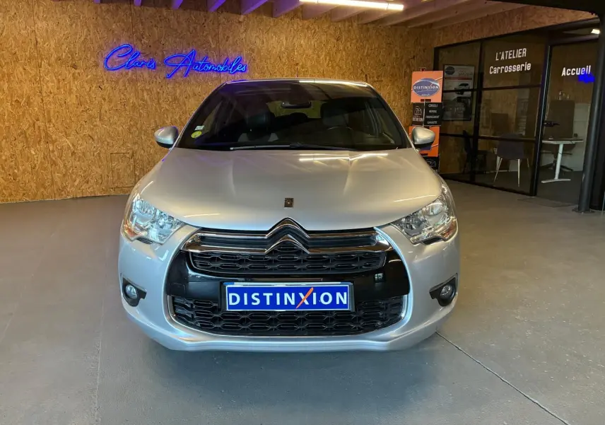 Vue avant d'une DS4 gris clair diesel de 2014, avec calandre noire et logo Citroën, en intérieur showroom.
