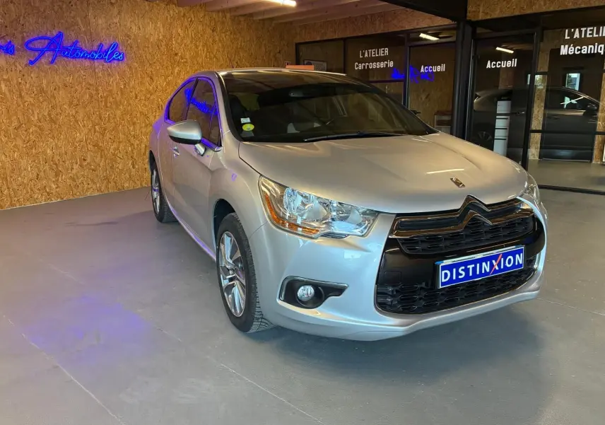 Vue 3/4 avant droite d'une DS4 gris clair diesel de 2014, avec calandre noire et phares distinctifs, en intérieur showroom.