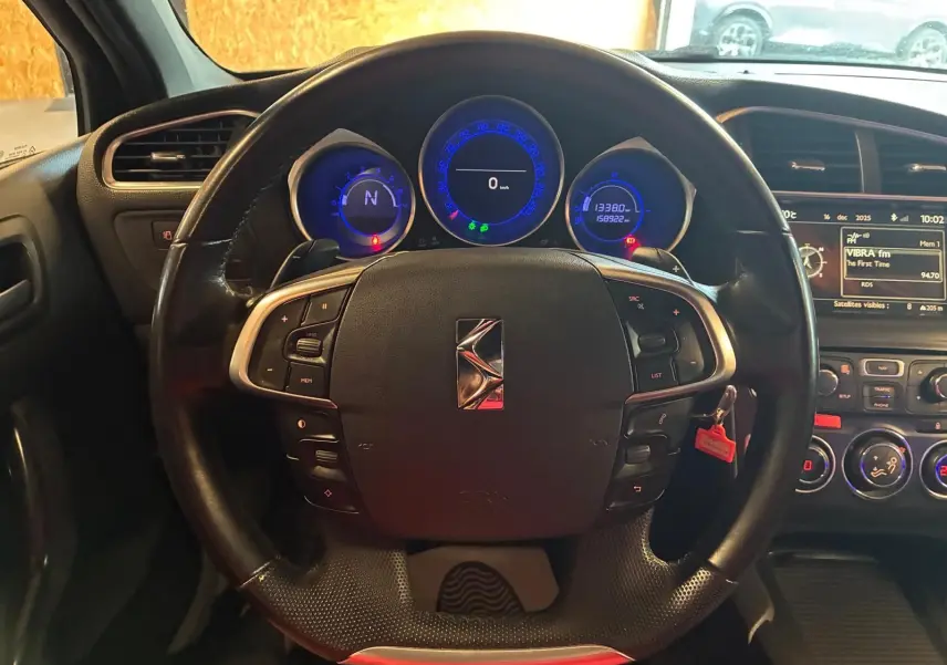 Vue intérieure centrée sur le volant noir du DS4 gris, avec tableau de bord et compteurs lumineux bleus en arrière-plan.