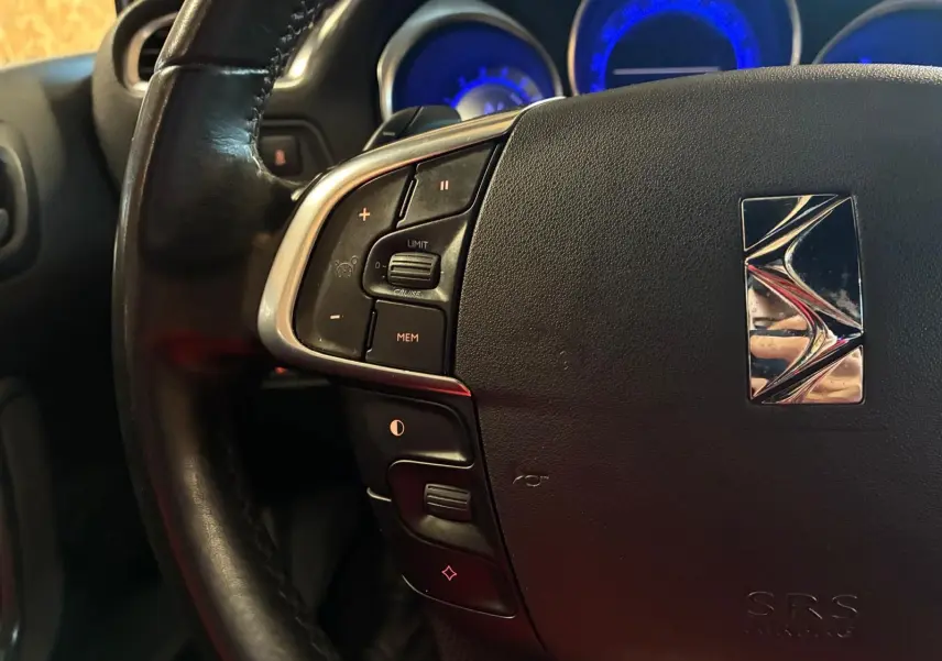 Gros plan sur le volant noir de la DS4 2014 avec commandes intégrées et tableau de bord éclairé en bleu.