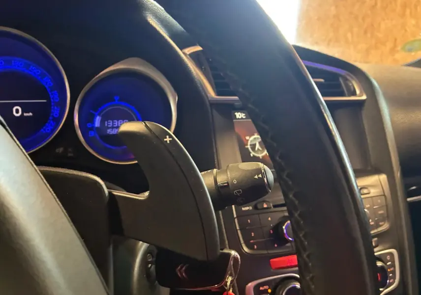 Gros plan sur le volant et le tableau de bord du DS4 gris, avec affichage digital bleu et commande de boîte auto visible.