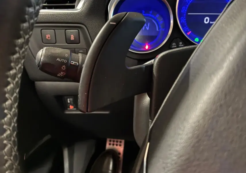 Gros plan sur la palette de changement de vitesse côté droit du volant d’un DS4 gris, avec compteurs bleus en arrière-plan.