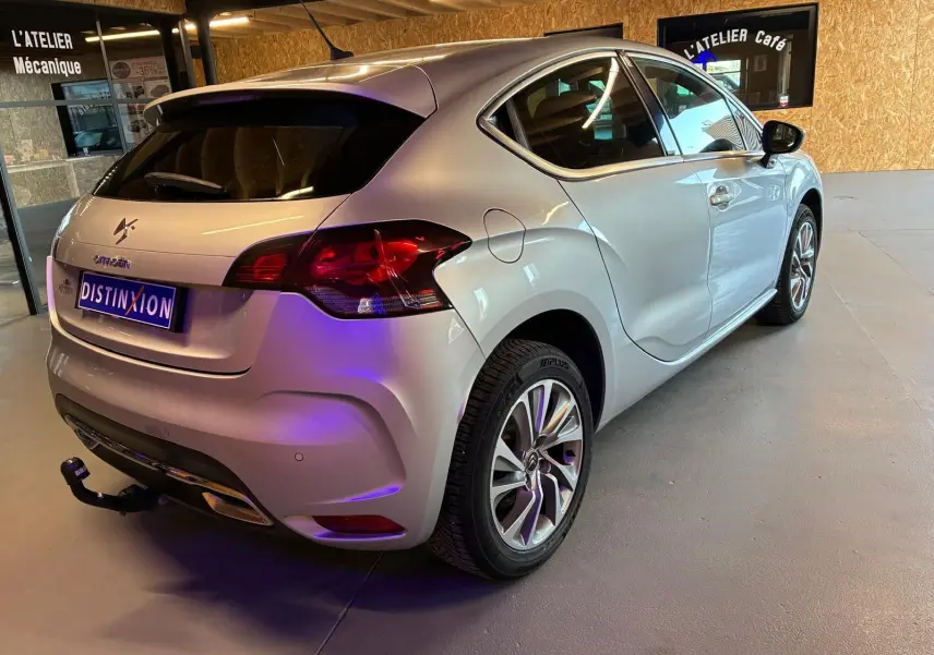 Vue 3/4 arrière droite d'une DS4 gris clair avec hayon, jantes alliage et attelage dans un garage intérieur.