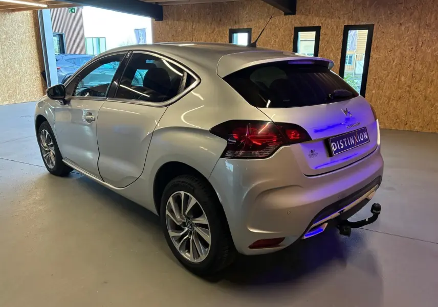 Vue 3/4 arrière droite d'une DS4 gris métallisé avec hayon, feux arrière LED et attelage visible en intérieur lumineux.