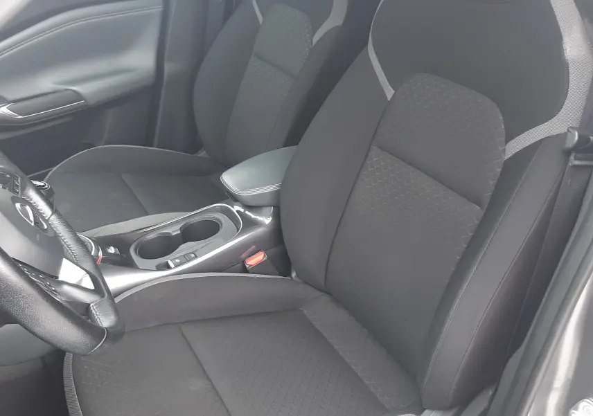 Vue intérieure côté conducteur du Nissan Juke 2020 gris, sièges tissu noir avec surpiqûres grises et accoudoir central.