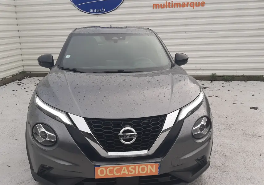 Vue avant d'un Nissan Juke gris 2020 avec calandre en V chromée et phares LED distinctifs sous la pluie.