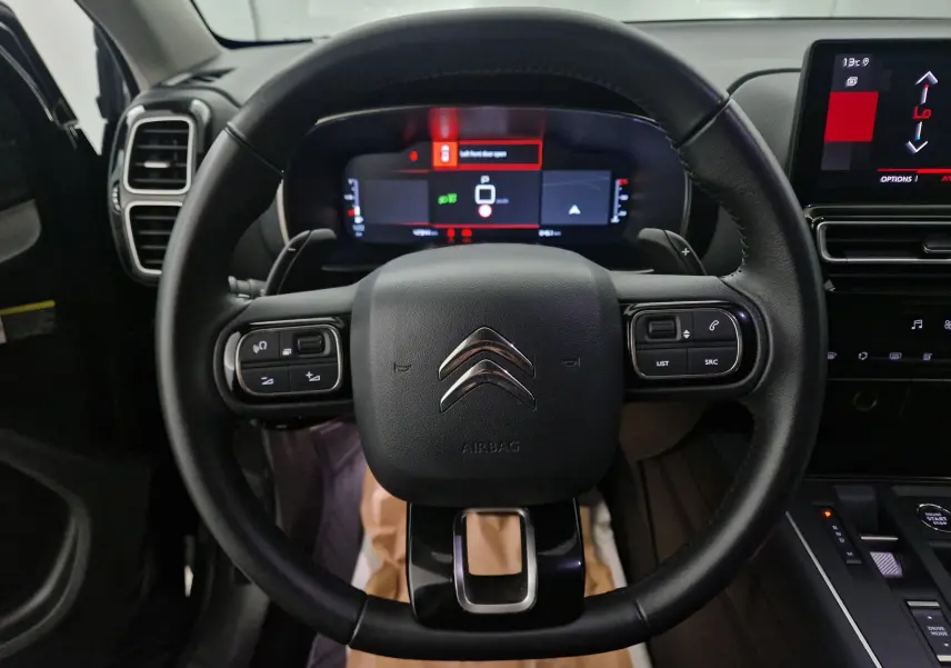 Vue rapprochée du volant noir de la Citroën C5 Aircross 2024 avec tableau de bord numérique et écran tactile central.