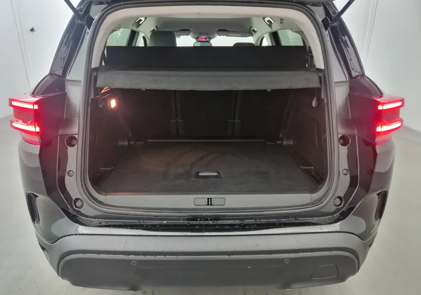 Coffre ouvert vu de l'arrière d'un Citroën C5 Aircross noir 2024 avec feux arrière allumés et cache-bagages en place.