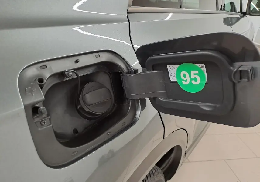 Gros plan sur la trappe à carburant ouverte côté gauche d'un Volkswagen T-Roc gris Indium 2024 avec étiquette essence 95 visible.