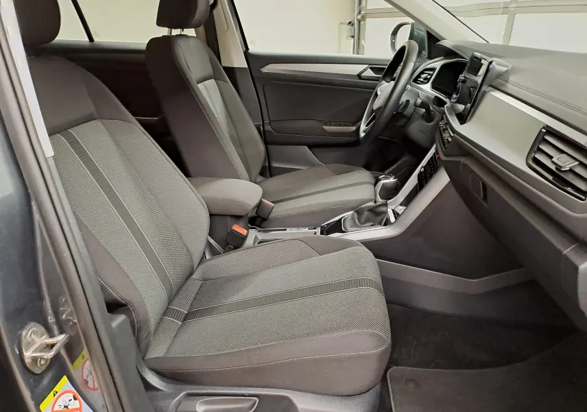 Intérieur avant droit du Volkswagen T-Roc 2024, sièges tissu gris et console centrale avec boîte automatique.