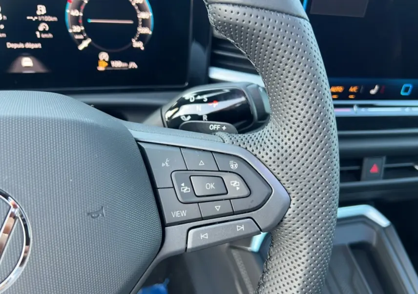 Gros plan sur le volant cuir perforé côté droit du Volkswagen T-Roc gris loup avec commandes multifonctions et tableau de bord numérique.