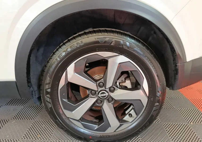 Gros plan sur la roue avant droite du Nissan Qashqai blanc, jante alliage au design moderne et pneu Nexen visible.