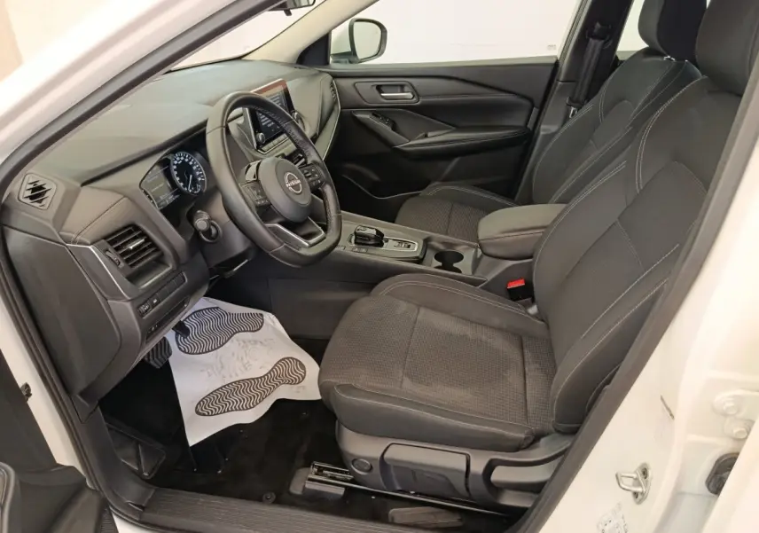 Intérieur avant droit du Nissan Qashqai blanc 2024, avec sièges noirs, volant multifonctions et console centrale moderne.
