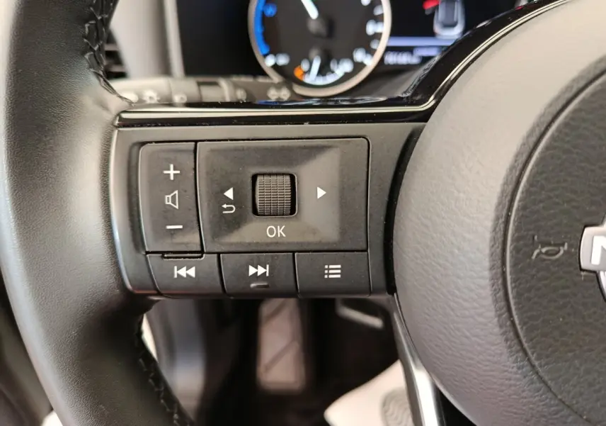 Gros plan sur les commandes gauche du volant noir du Nissan Qashqai e-Power 2024 avec tableau de bord partiellement visible.