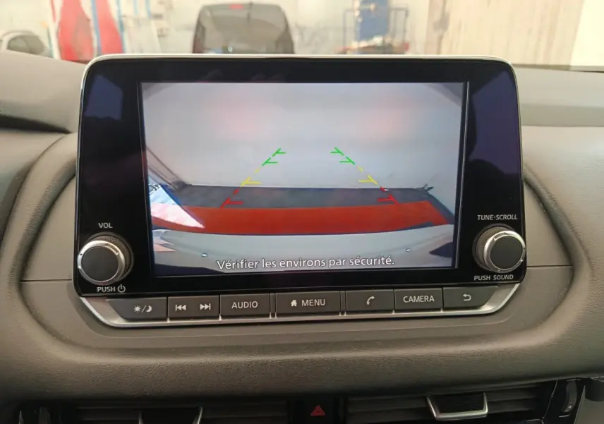Écran central affichant la caméra de recul du Nissan Qashqai blanc, avec lignes de guidage colorées.