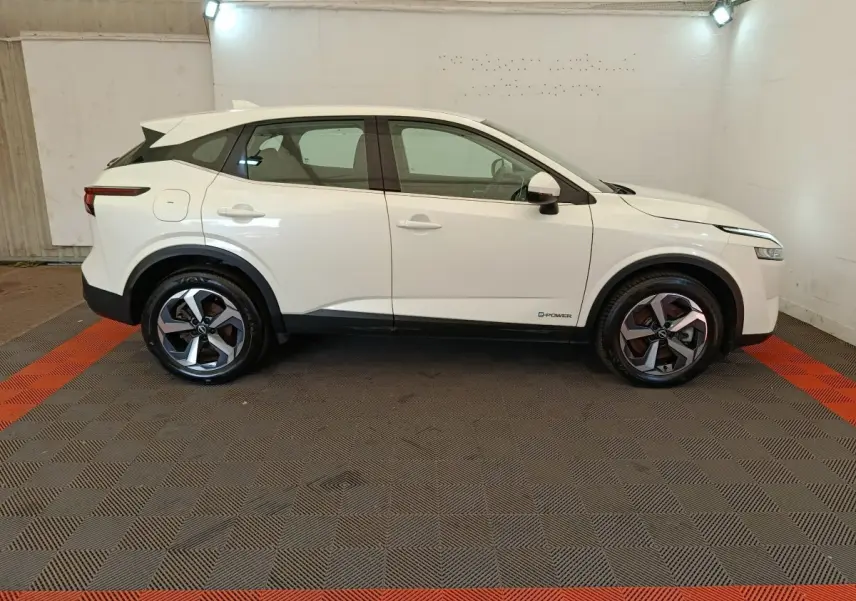 Vue de profil côté gauche d'un Nissan Qashqai e-Power blanc avec jantes alliage et toit noir dans un garage.