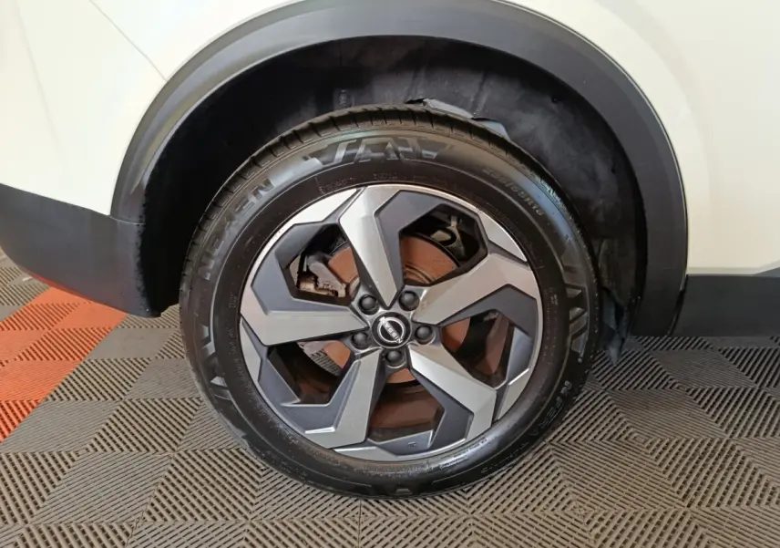 Gros plan sur la roue avant droite du Nissan Qashqai blanc 2024 avec jante alliage gris et logo Nissan au centre.