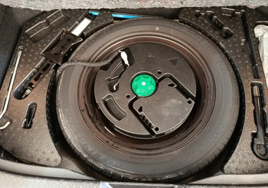 Vue plongeante sur la roue galette noire et ses outils de secours dans le coffre du Nissan Qashqai blanc 2024.