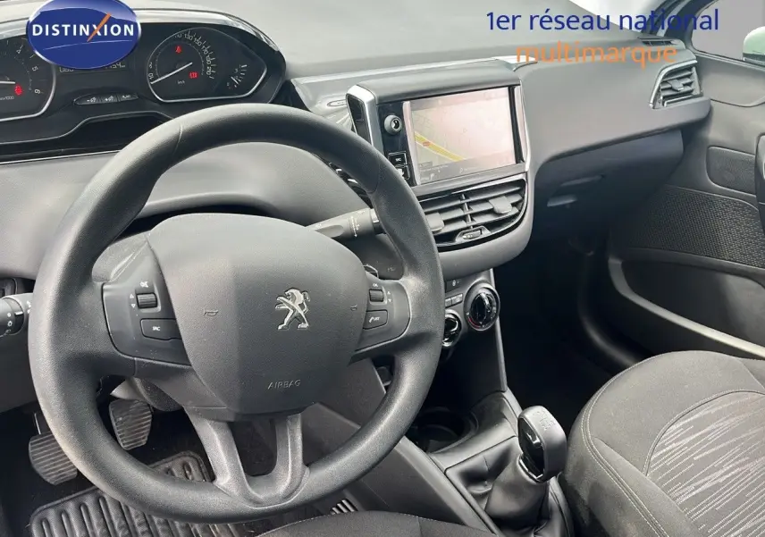 Vue intérieure du poste de conduite de la Peugeot 208 blanche, avec volant, tableau de bord et écran tactile central visibles.