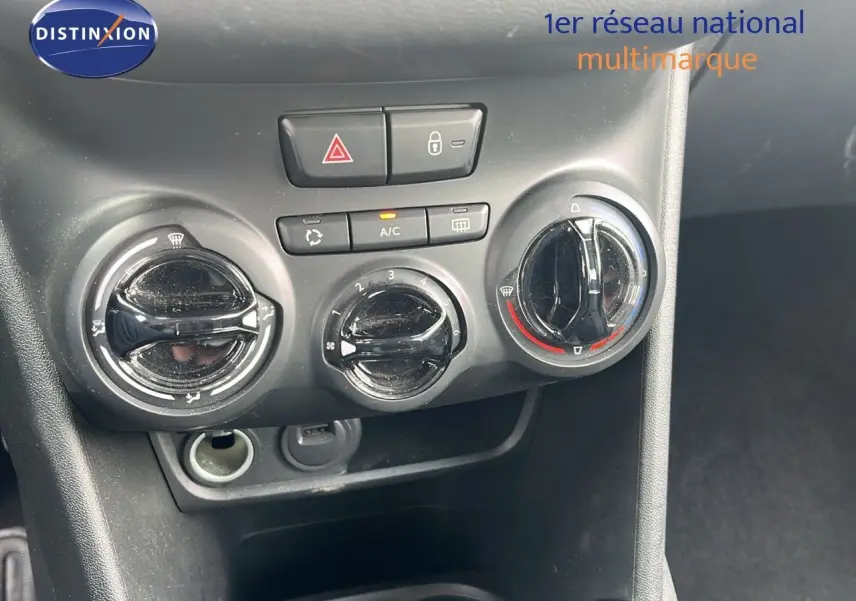 Gros plan sur les commandes de climatisation et les boutons de sécurité du tableau de bord d'une Peugeot 208 blanche.