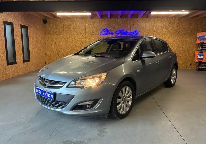 Opel Astra gris 2015 vue 3/4 avant droit avec phares allumés dans un showroom intérieur.