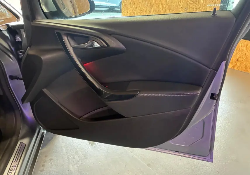 Vue intérieure de la porte côté gauche d'une Opel Astra gris 2015, avec garniture noire et surpiqûres blanches.