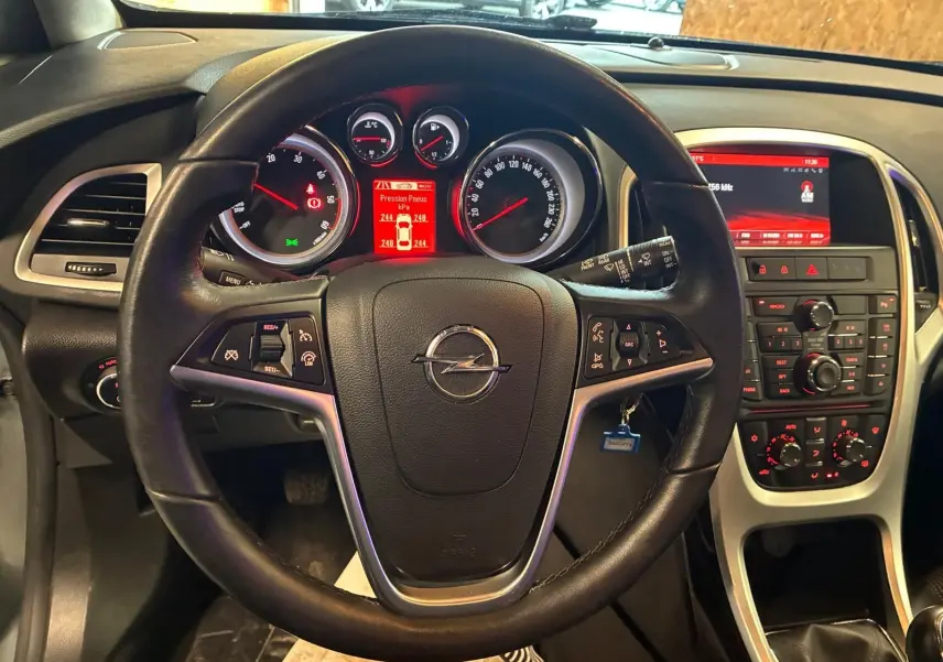 Vue intérieure centrée sur le volant noir d'une Opel Astra 2015 avec tableau de bord et console centrale rétroéclairés en rouge.