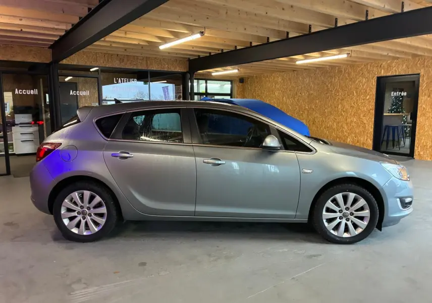 Vue de profil côté gauche d'une Opel Astra gris métallisé de 2015 stationnée dans un garage avec murs en bois.