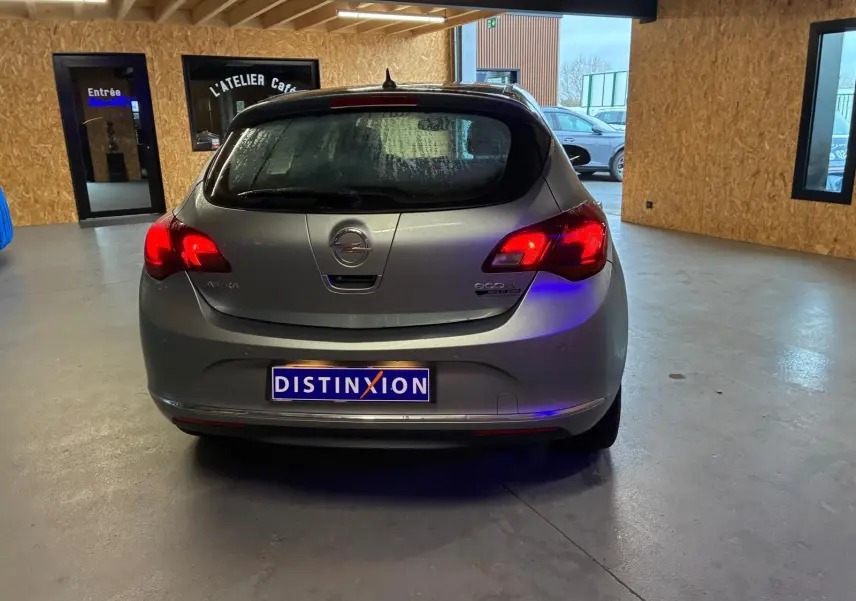 Vue arrière d'une Opel Astra gris métallisé de 2015 avec feux allumés dans un garage intérieur.