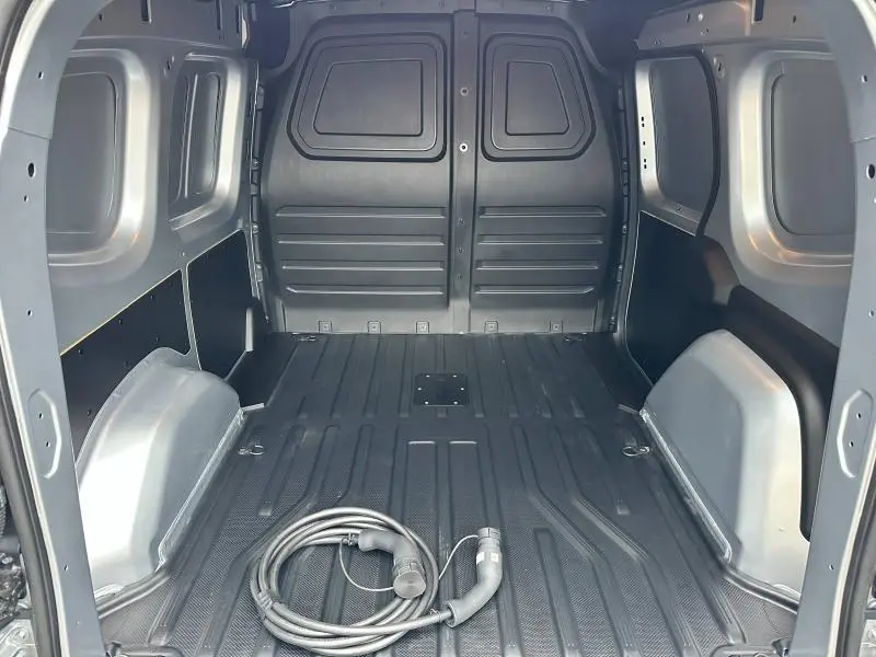 Intérieur de la zone de chargement du Nissan Townstar gris 2024, vue arrière avec câble de recharge électrique au sol.