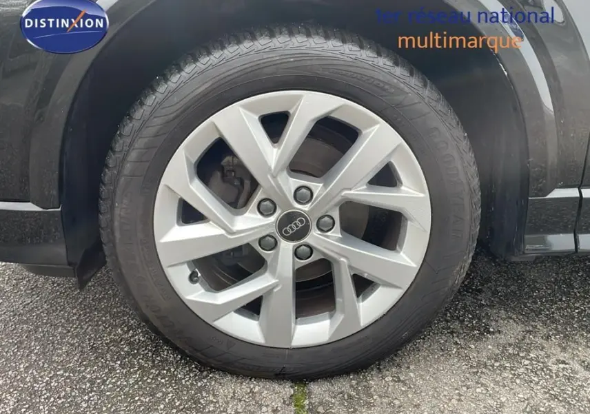 Gros plan sur la roue avant gauche d'un Audi Q2 noir mito metal avec jante alliage 17 pouces et logo Audi central.