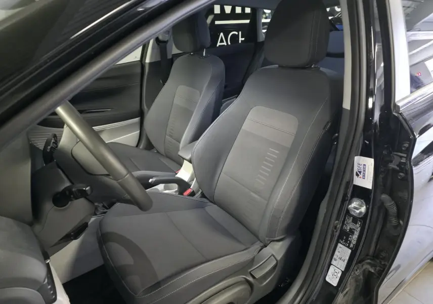 Vue intérieure côté conducteur du Hyundai Bayon noir 2025, sièges tissu gris et accoudoir central coulissant visible.