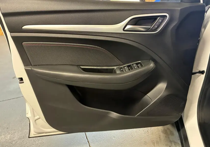 Vue de la porte avant gauche ouverte d’un MG ZS blanc 2022, intérieur noir avec commandes de vitres et poignée intégrée.